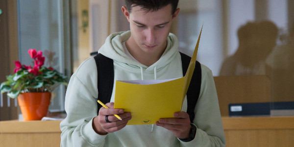 A highschooler is reading paper handouts while holding a pencil
