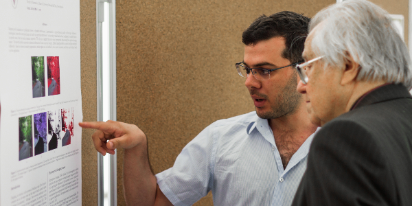 Two people talking in front of a bulletin board with a research paper poster